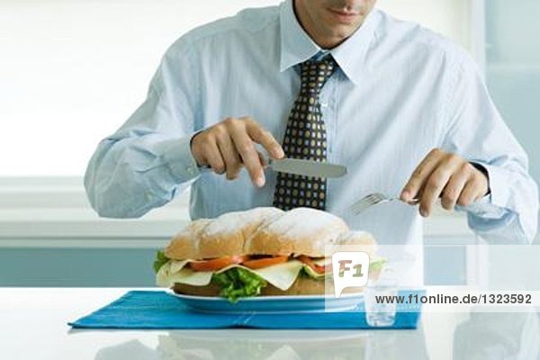 Mann isst großes Sandwich mit Messer und Gabel