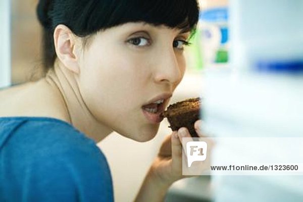 Frau isst ein Stück Schokoladenkuchen  schaut über die Schulter in die Kamera