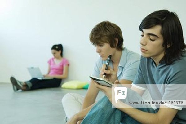 Teenager-Freunde sitzen auf dem Boden,  einer schreibt in ein Notizbuch.