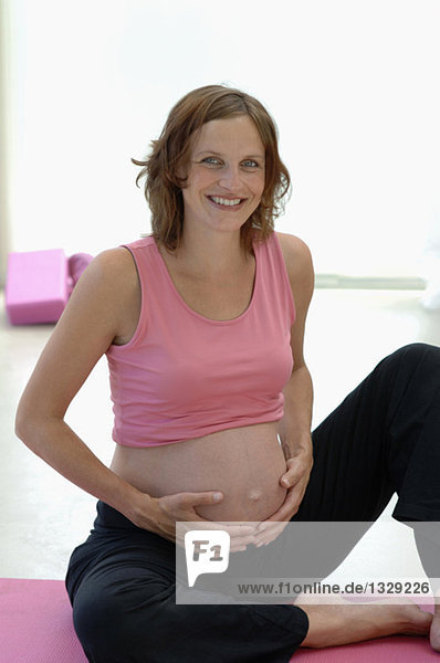 Schwangere Frau auf Yogamatte sitzend