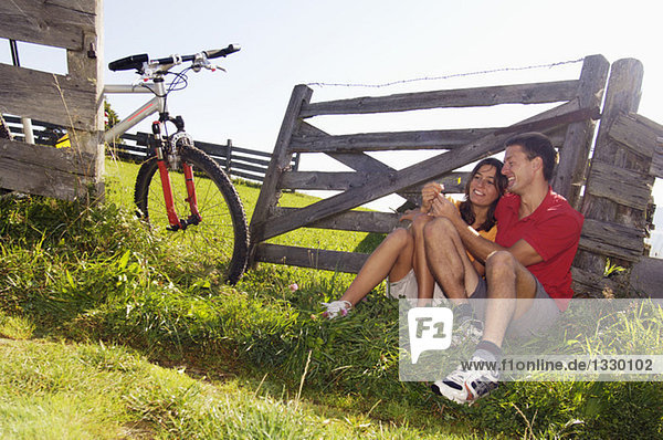 Couple sitting in meadow,  leaning on wooden railing