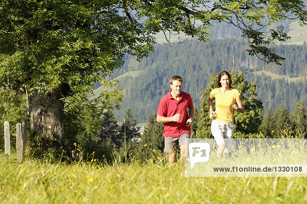 Young couple jogging in meadow  mountains in background