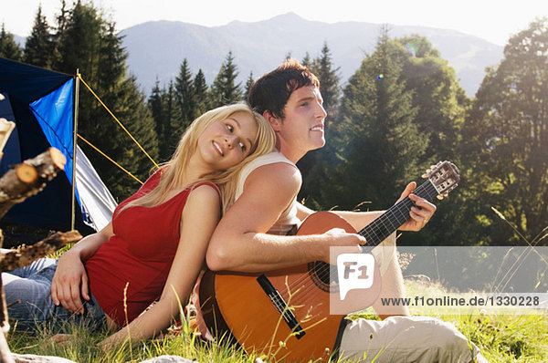 Junges Paar auf der Wiese sitzend  Mann spielt Gitarre