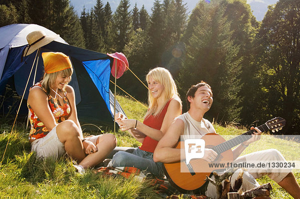 Three young people having picnic  man playing guitar