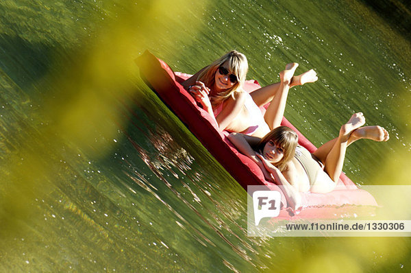 Zwei Teenager-Mädchen (16-17) schwimmend auf dem Luftbett im See  Neigungsansicht