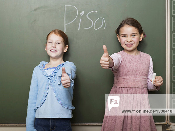 Girls (4-7) standing by blackboard  showing thumbs up sign