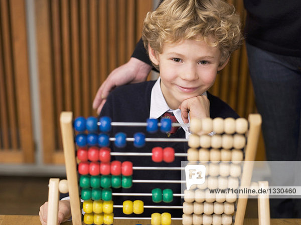 Boy (4-7) sitting by abacus  hand on chin  smiling
