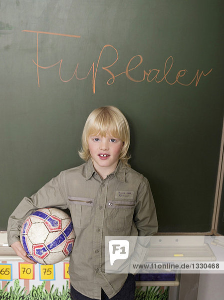 Junge (4-7) steht vor der Tafel  hält Fußball  Porträt