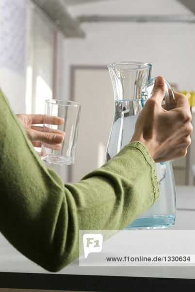 Junge Frau gießt Wasser aus der Kanne ins Glas  Mittelteil  Nahaufnahme