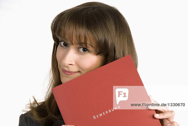 Junge Frau mit Gesicht von Bewerbungsmappe bedeckt  lächelnd  Portrait