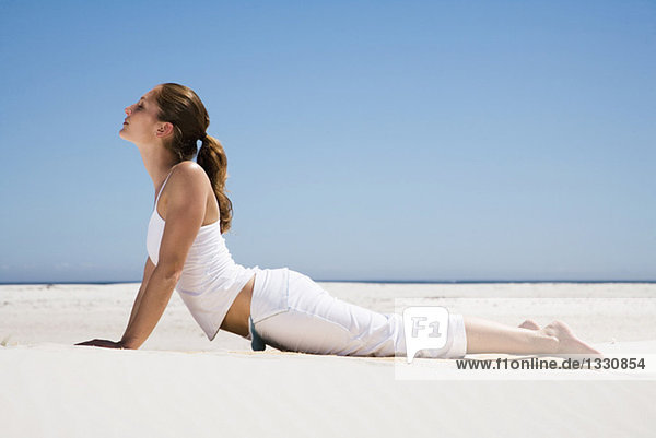 Junge Frau beim Yoga am Strand  Seitenansicht