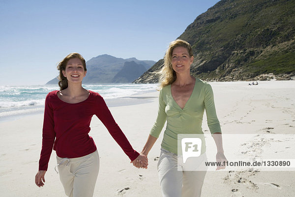 Mutter und Tochter gehen Hand in Hand am Strand.