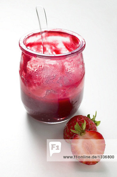 Glas Erdbeermarmelade mit Löffel  daneben frische Erdbeeren