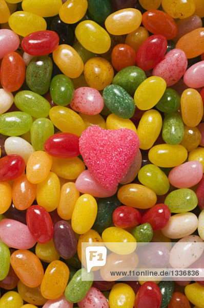 Bunte Jelly Beans und ein rosa Zuckerherz (bildfüllend)