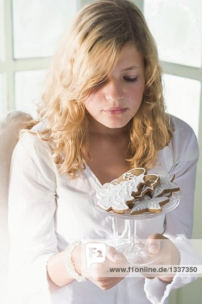 Blond girl holding glass bowl of assorted gingerbread biscuits