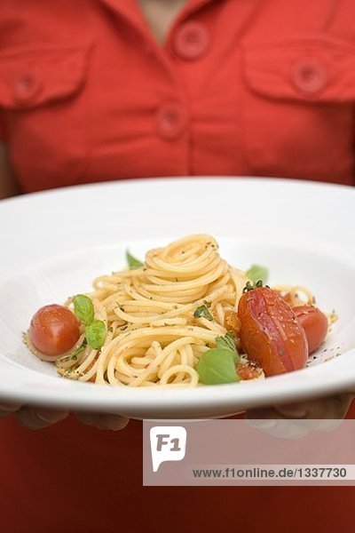 Frau hält Teller Spaghetti mit Tomaten und Basilikum