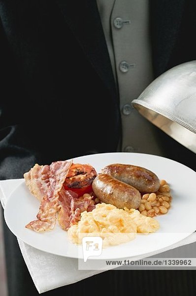 Butler serving English breakfast on plate with dome cover