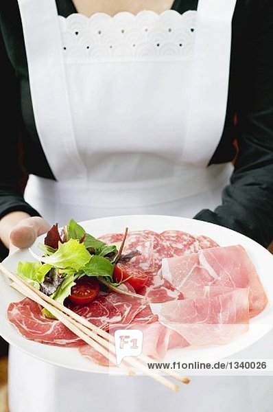 Kellnerin serviert italienische Wurstplatte mit Grissini
