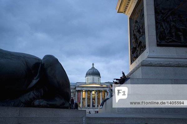 Tourists sitting on steps of monument at city square  Trafalgar Square  Westminster  London  England