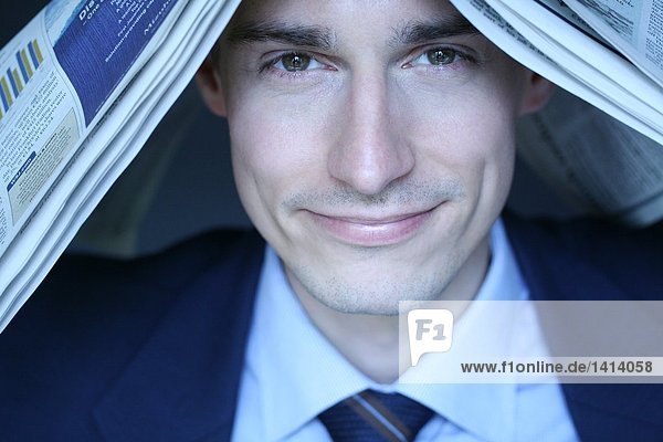 Close-up of businessman with newspaper on his head and smiling