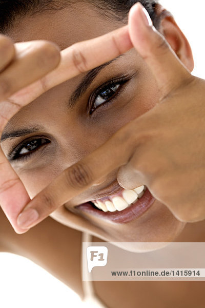Porträt einer jungen lächelnden Frau  die mit den Fingern einen Rahmen macht.