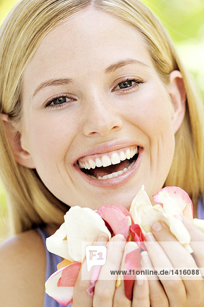 Porträt einer jungen blonden Frau  die lächelt und Blütenblätter hält  im Freien