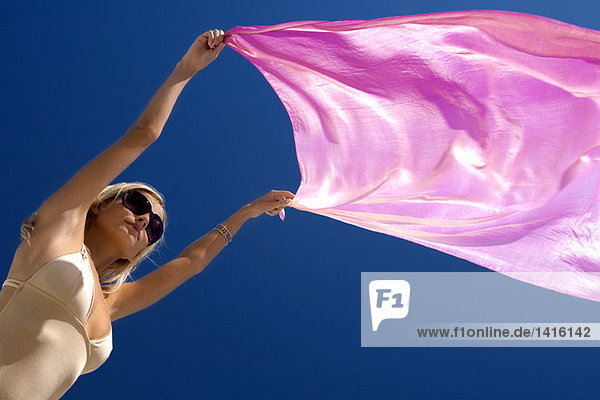 Junge Frau in Badeanzug mit rosa Pareo im Wind