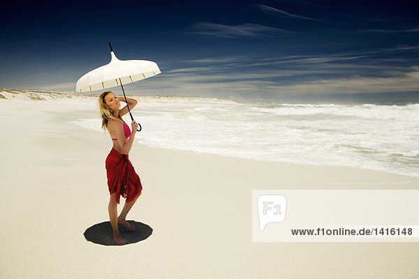 Junge Frau im Bikini und Pareo mit Sonnenschirm am Strand