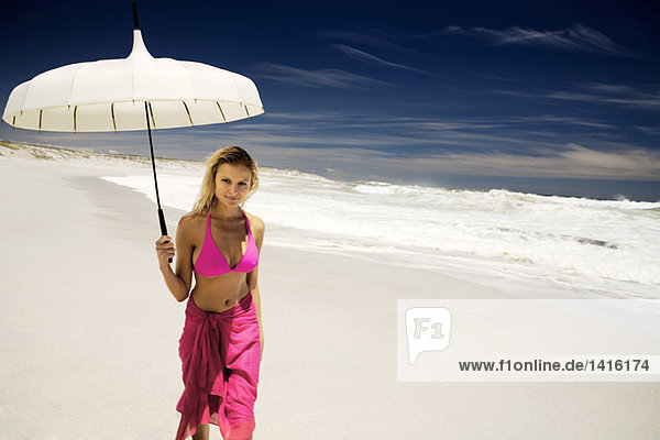 Junge Frau im Bikini und Pareo mit Sonnenschirm am Strand