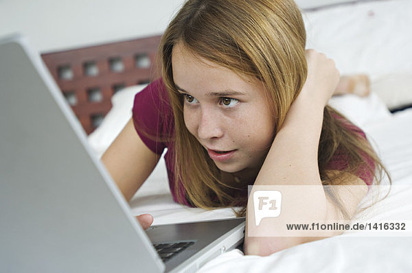 Teenager Mädchen auf dem Bett liegend  mit Laptop