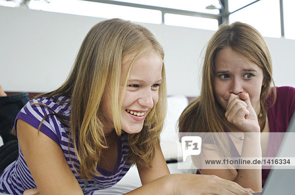 2 lächelnde Teenager-Mädchen auf dem Bett liegend  mit Laptop