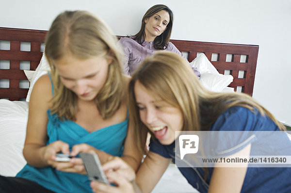 2 lächelnde Teenager-Mädchen mit Mobiltelefonen  Frau im Hintergrund