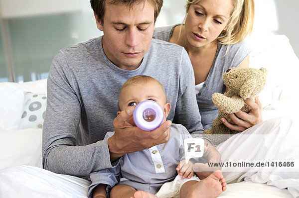 Junges Paar und Baby sitzend im Haus  Vater füttert seinen Sohn