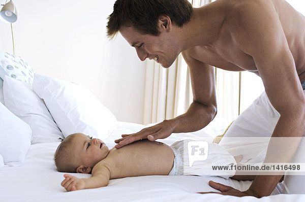 Vater streichelt Brustkorb-Baby  liegt auf einem Bett  drinnen