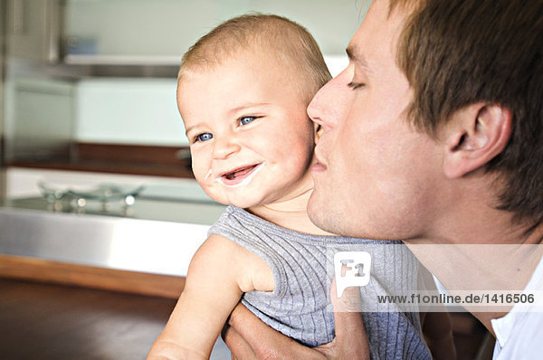 Portrait of father and son in kitchen  man kissing his baby  indoors