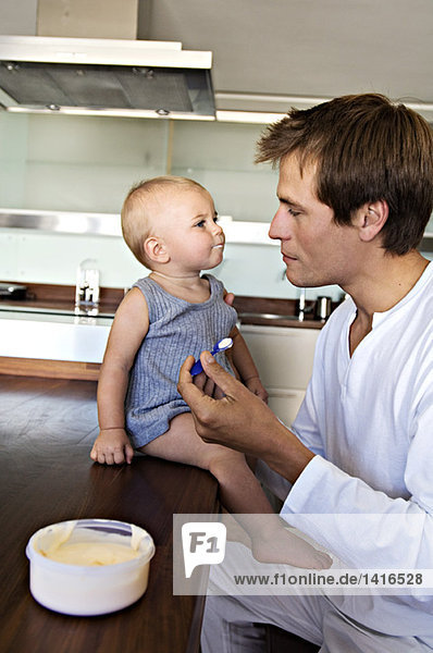 Father and son in kitchen  man feeding his baby  indoors