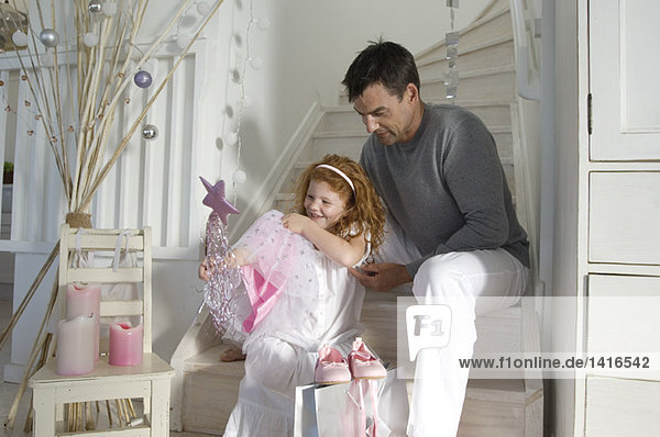 Father and daughter opening Christmas presents  girl holding a princess costume  indoors