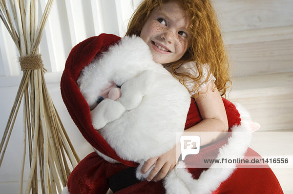 Weihnachtstag  Porträt eines kleinen Mädchens mit Kuscheltier (Weihnachtsmann)  drinnen
