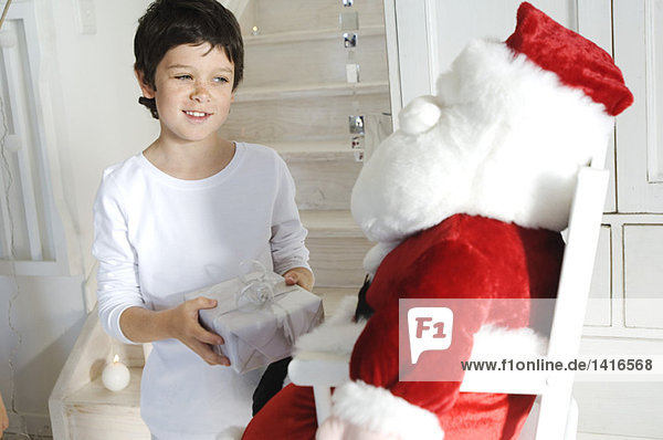 Little boy holding a present  looking at a cuddly toy (Santa Claus)  indoors