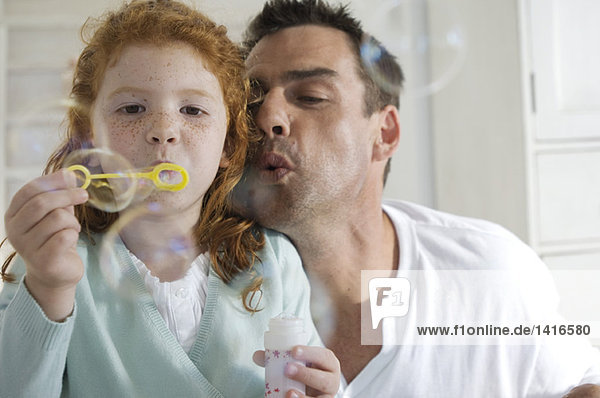 Father and daughter making soap bubbles  indoors