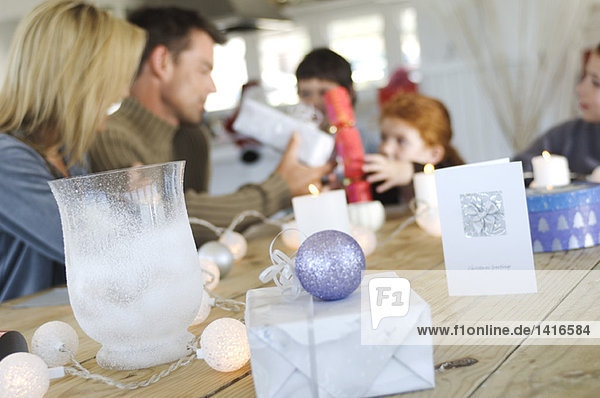 Couple and three children sitting around table  exchanging Christmas presents  indoors