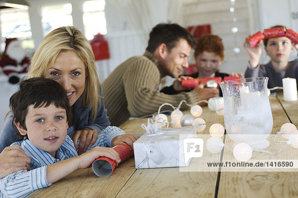 Couple and three children sitting around table  exchanging Christmas presents  indoors