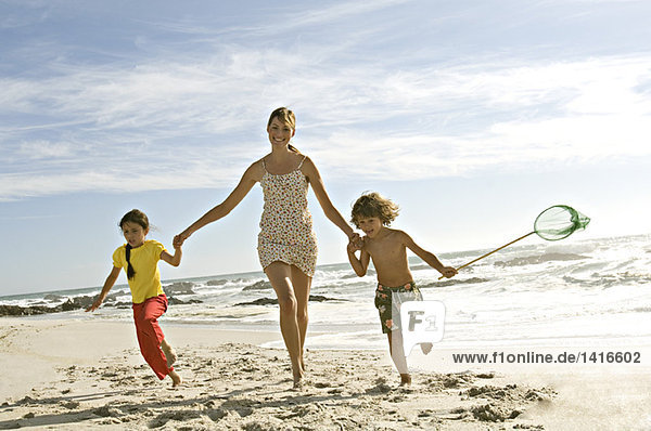 Mutter und zwei Kinder rennen am Strand  im Freien