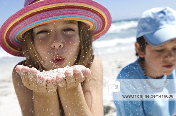 Portrait of a little girl blowing sand in her hands  boy in background  outdoors