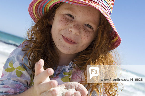 Porträt eines kleinen Mädchens  das lächelnd in die Kamera schaut  Sand in den Händen  im Freien