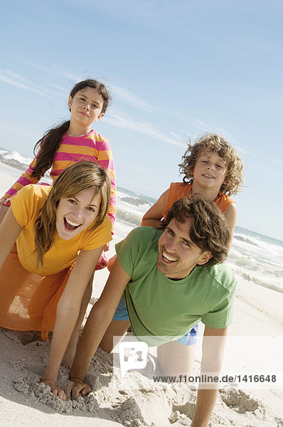Eltern und zwei Kinder spielen am Strand und halten Tochter und Sohn auf dem Rücken  im Freien.