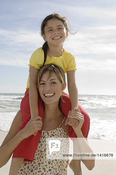 Porträt einer Mutter  die ihre Tochter in den Schultern  am Strand und im Freien trägt.