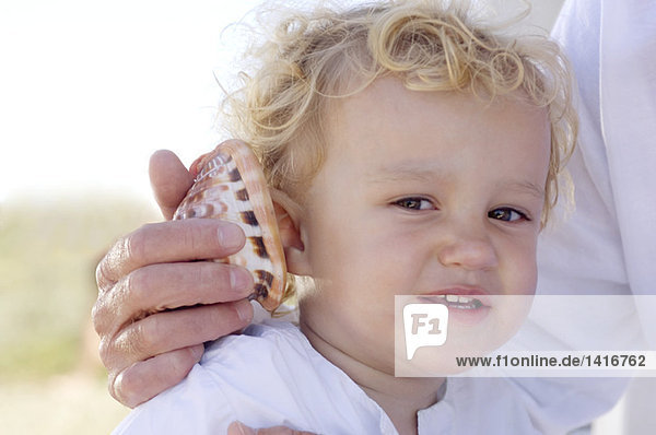 Porträt eines kleinen Jungen mit einer Muschel am Ohr