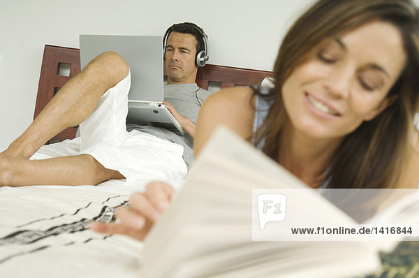 Paar auf dem Bett  Frau liest  Mann mit Laptop  drinnen