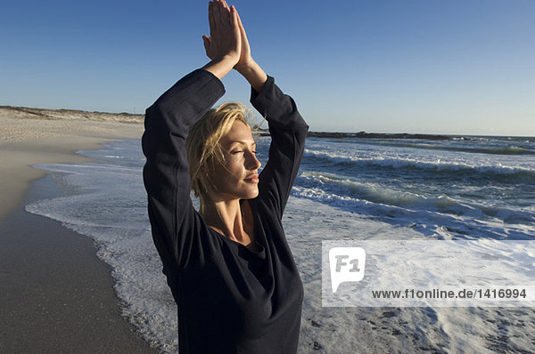 Junge Frau in Yogahaltung am Strand  im Freien